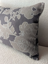 Cargar imagen en el visor de la galería, A square decorative throw pillow with a gray and white floral pattern, resting on a textured beige fabric surface.